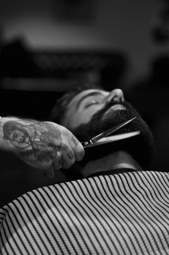 Fotografía de una persona recostada a la que le estan cortando la barba con unas tijetas